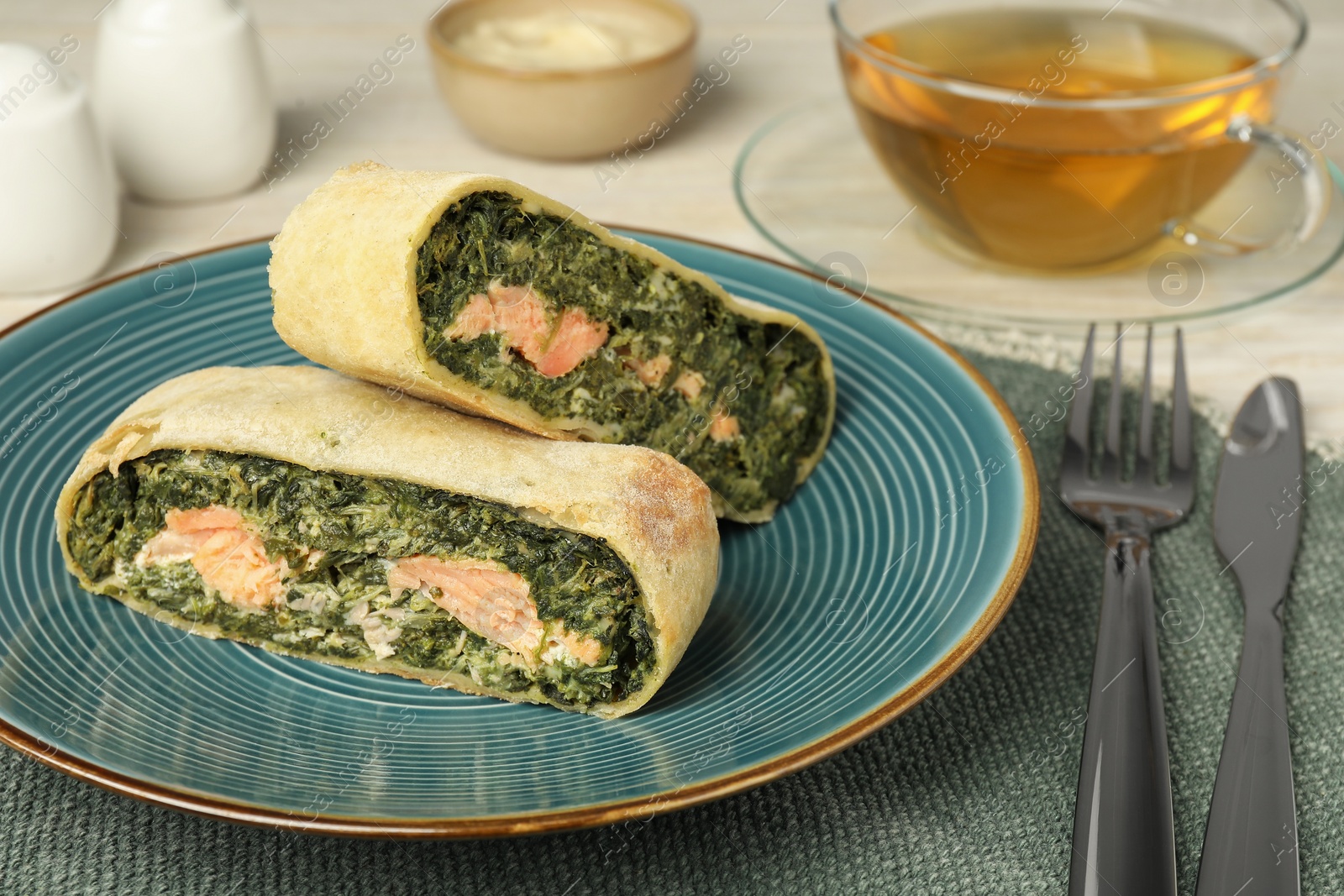 Photo of Pieces of delicious strudel with salmon and spinach served on table, closeup