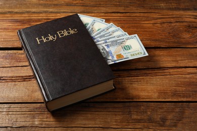 Photo of Holy Bible and money on wooden table. Space for text