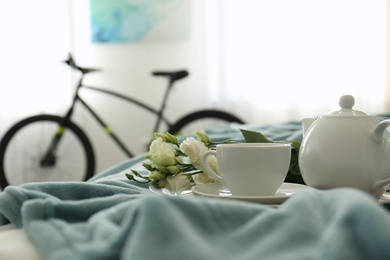 Photo of Stylish room interior with tea set on bed and modern bicycle