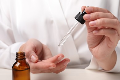 Photo of Woman applying cosmetic serum onto hand at white table, closeup