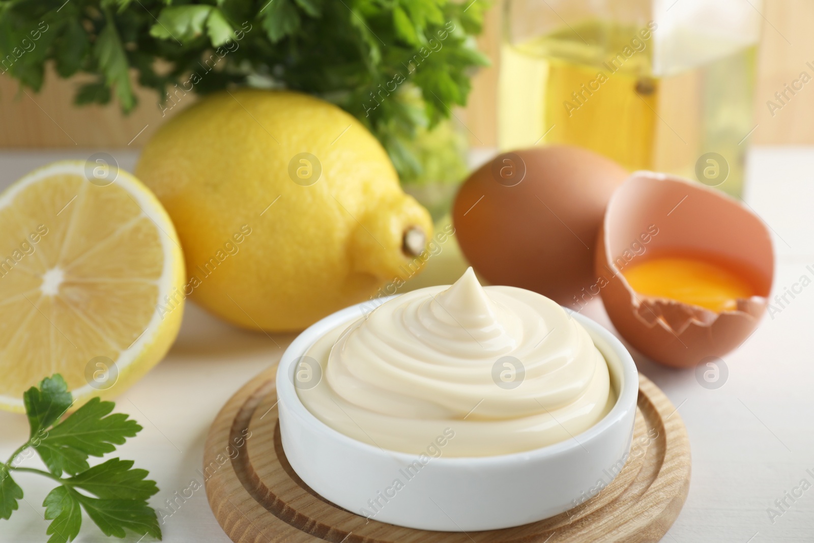 Photo of Fresh mayonnaise sauce in bowl and ingredients on white wooden table, closeup