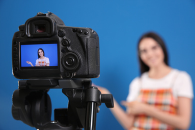 Photo of Young blogger recording video against blue background, focus on camera screen