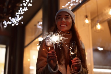 Photo of Happy young woman with sparkler and glass of champagne at winter fair