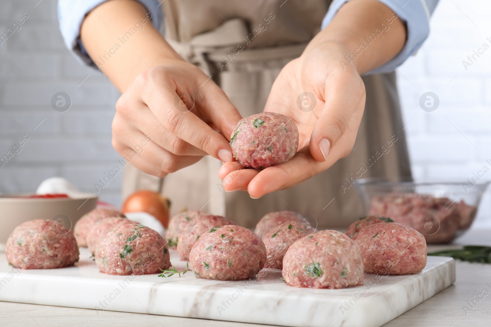 Photo of Woman making fresh raw meatballs at white table indoors, closeup