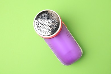Photo of Modern fabric shaver on light green background, top view