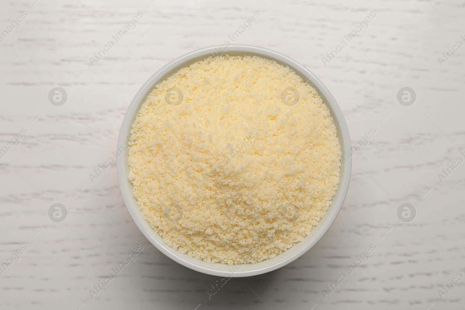 Photo of Delicious grated parmesan cheese in bowl on white wooden table, top view