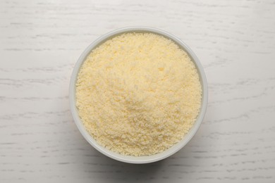 Photo of Delicious grated parmesan cheese in bowl on white wooden table, top view