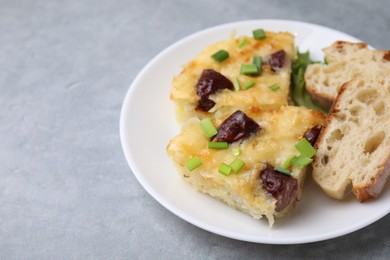 Photo of Tasty sausage casserole with green onion and bread on grey table, closeup. Space for text