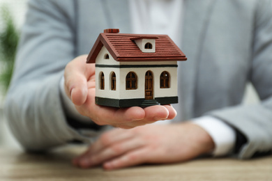 Photo of Real estate agent holding house model at wooden table, closeup