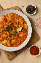 Delicious chicken curry and spices on wooden table, flat lay