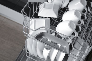 Photo of Open modern dishwasher with clean tableware, closeup