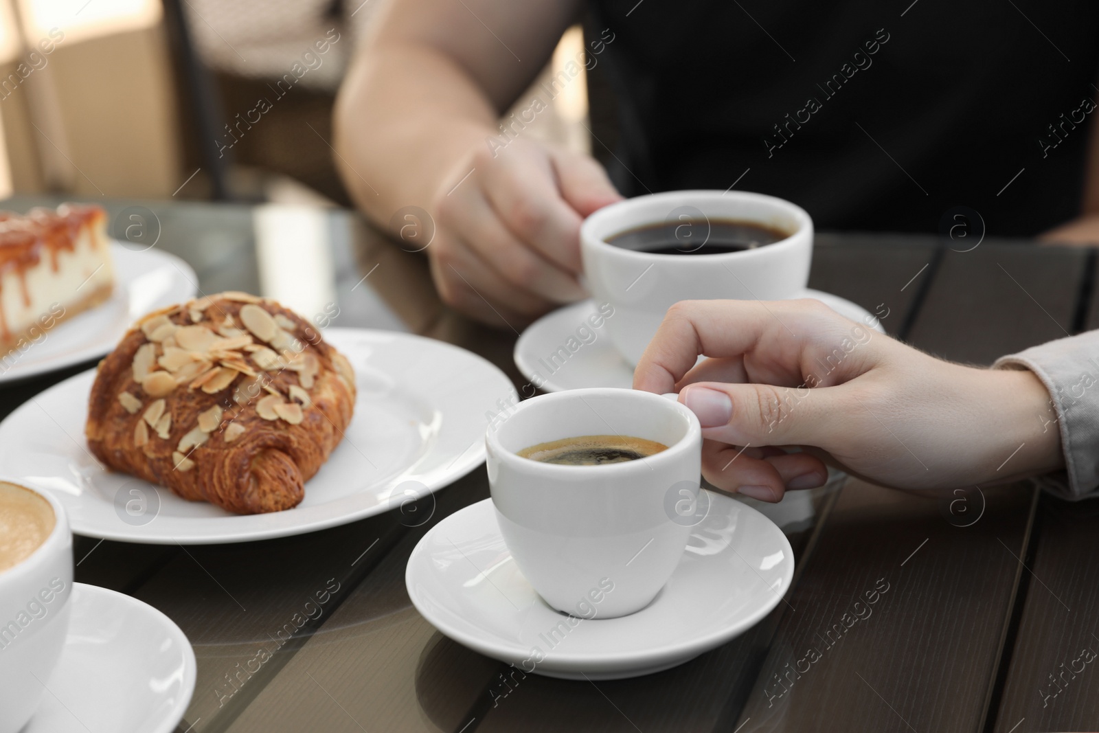 Photo of Friends drinking coffee at wooden table in outdoor cafe, closeup