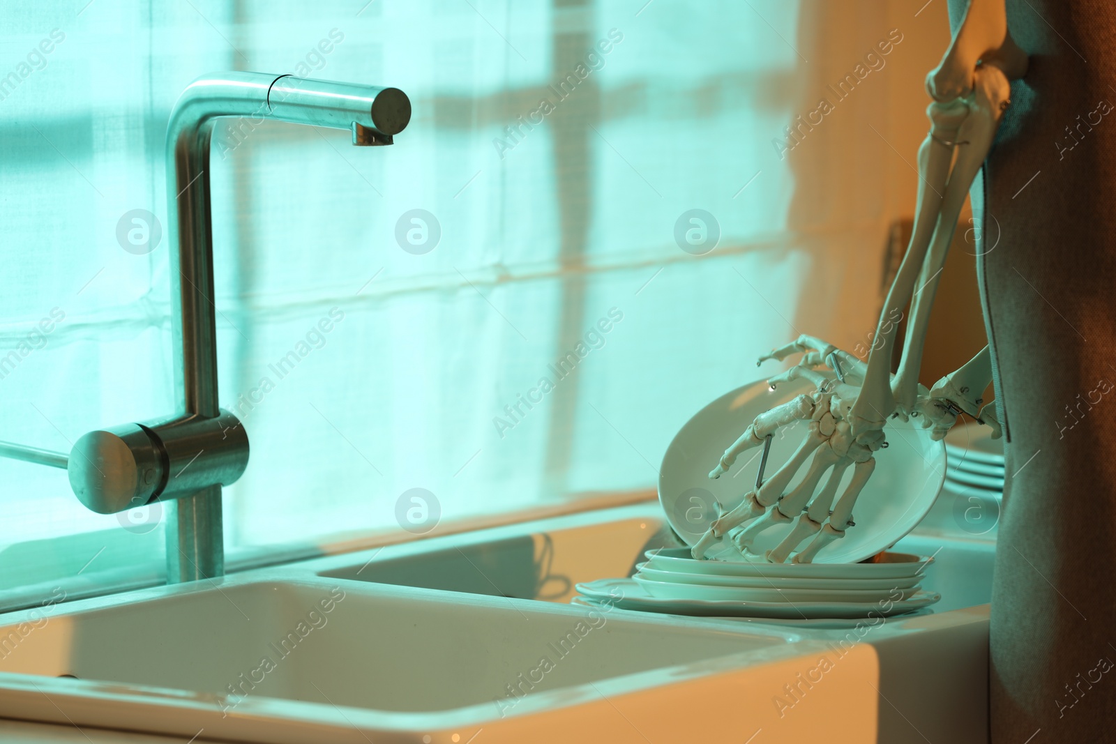 Photo of Human skeleton washing dishes in kitchen sink at night, closeup