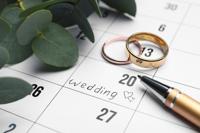 Photo of Calendar with date reminder about Wedding Day, pen and rings, closeup