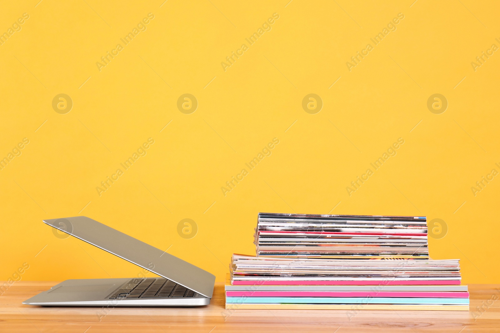 Photo of Laptop and stack of magazines on wooden table