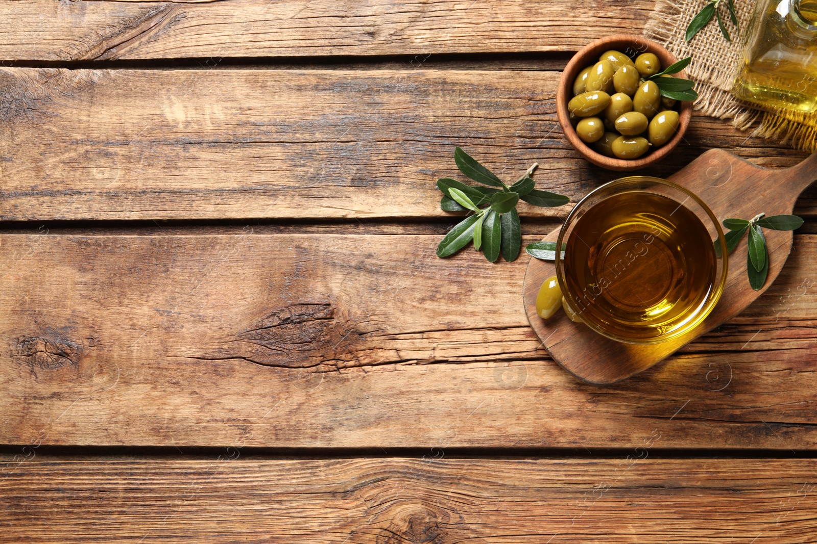 Photo of Glass bowl of fresh oil, ripe olives and green leaves on wooden table, flat lay. Space for text