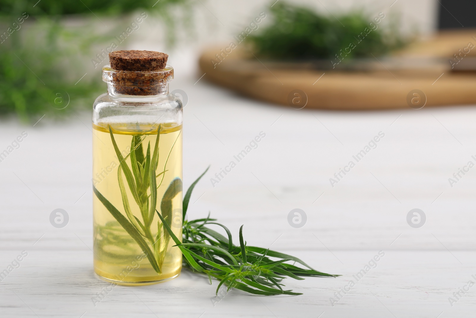 Photo of Bottle of essential oil and fresh tarragon leaves on white wooden table. Space for text