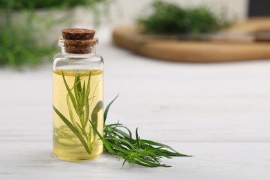 Photo of Bottle of essential oil and fresh tarragon leaves on white wooden table. Space for text