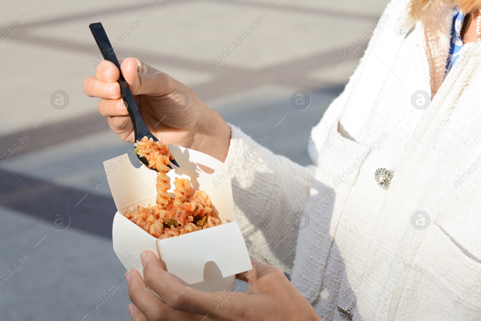 Photo of Woman eating takeaway noodles from paper box with fork outdoors, closeup. Street food