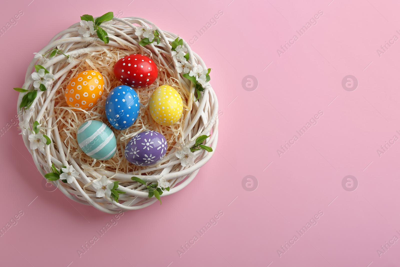 Photo of Nest with painted Easter eggs and space for text on color background, top view