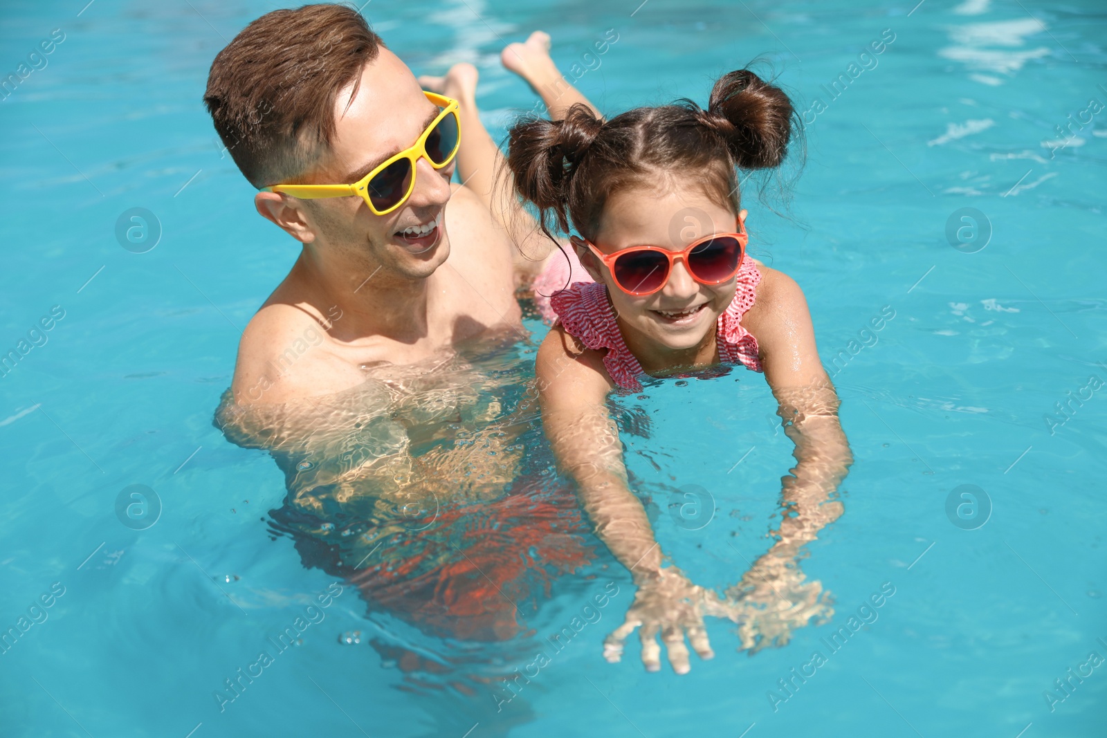 Photo of Young man teaching his daughter to swim in pool