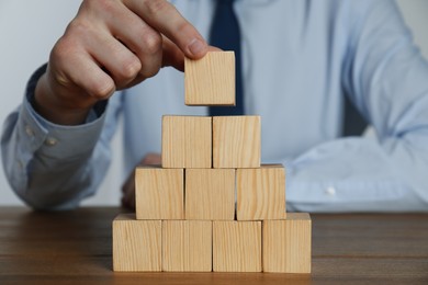 Businessman building pyramid of blank cubes on wooden table, closeup. Space for text