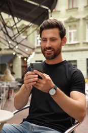 Photo of Handsome man using smartphone in outdoor cafe