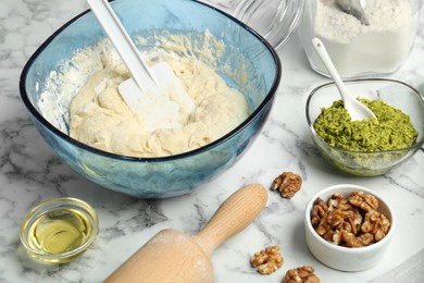 Photo of Making delicious pesto bread. Raw dough and ingredients on white marble table