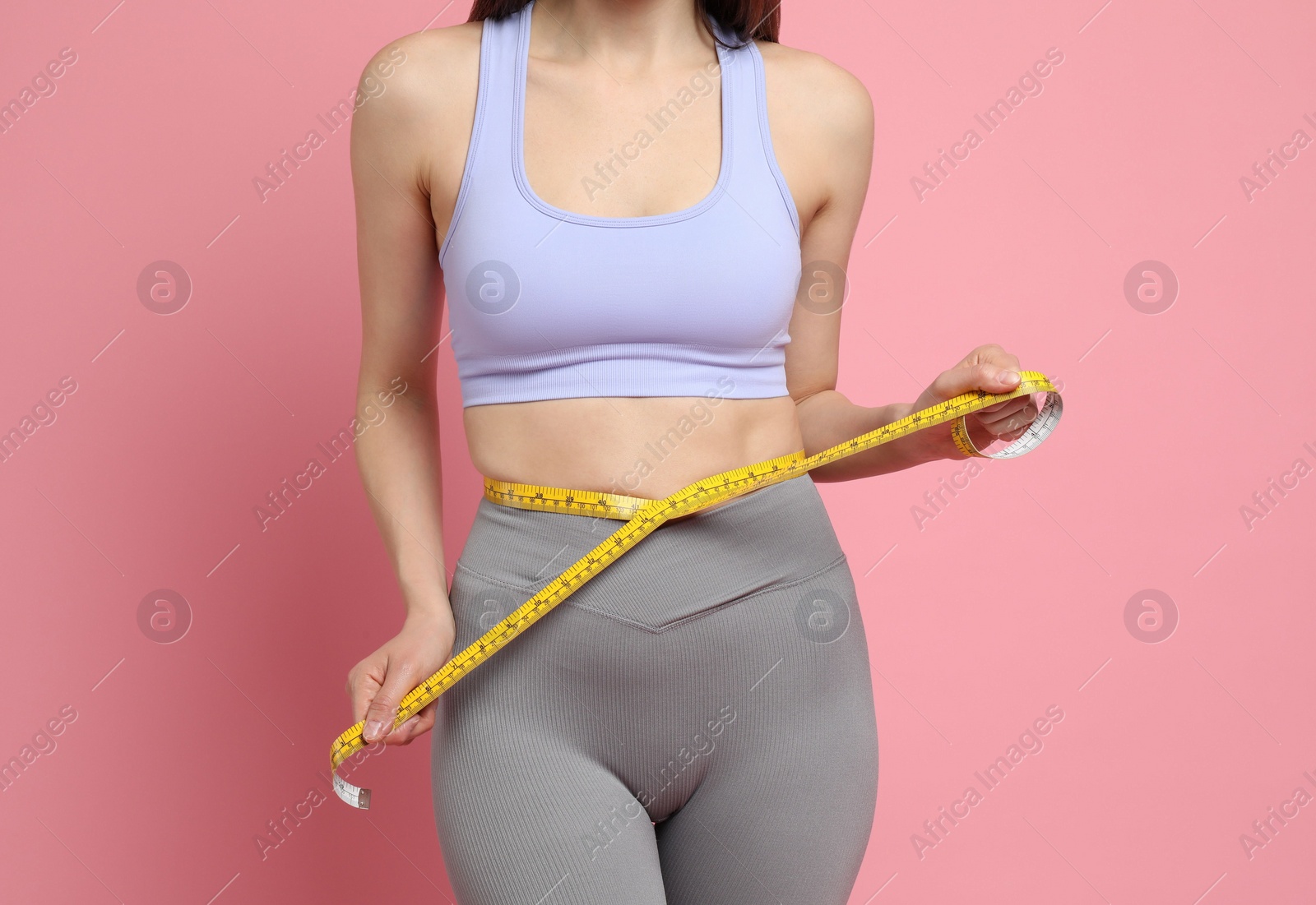 Photo of Woman with measuring tape showing her slim body on pink background, closeup