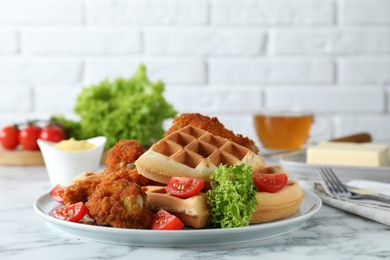 Photo of Tasty Belgian waffles served with fried chicken, tomatoes and lettuce on white marble table