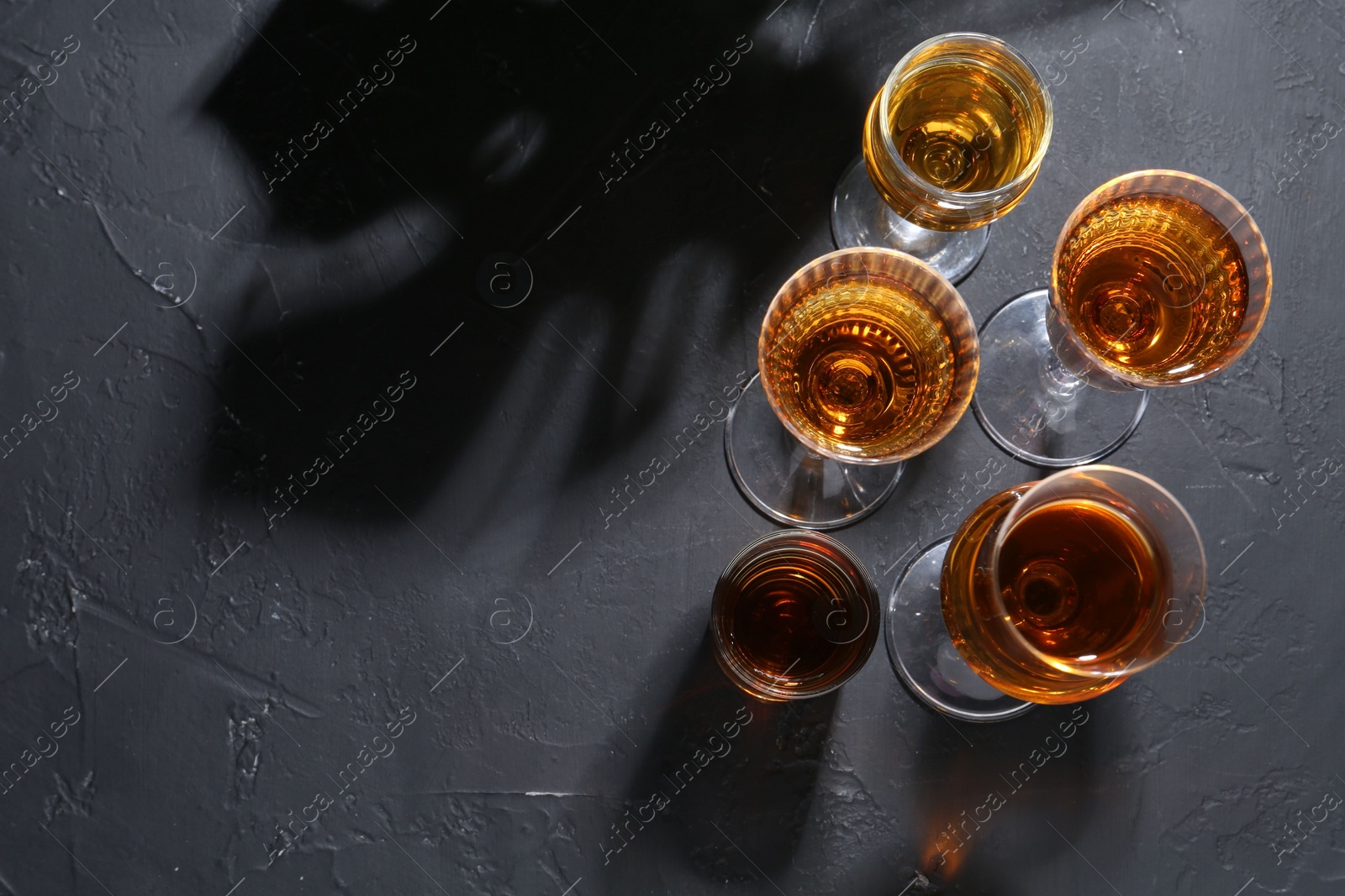 Photo of Many different liqueurs in glasses on dark textured table, flat lay. Space for text