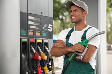 Worker with fuel pump nozzle at modern gas station