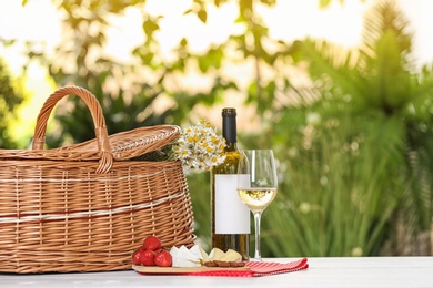 Picnic basket and wine with products on table against blurred background, space for text