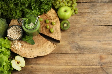 Photo of Mason jar of fresh green smoothie and ingredients on wooden table, flat lay. Space for text