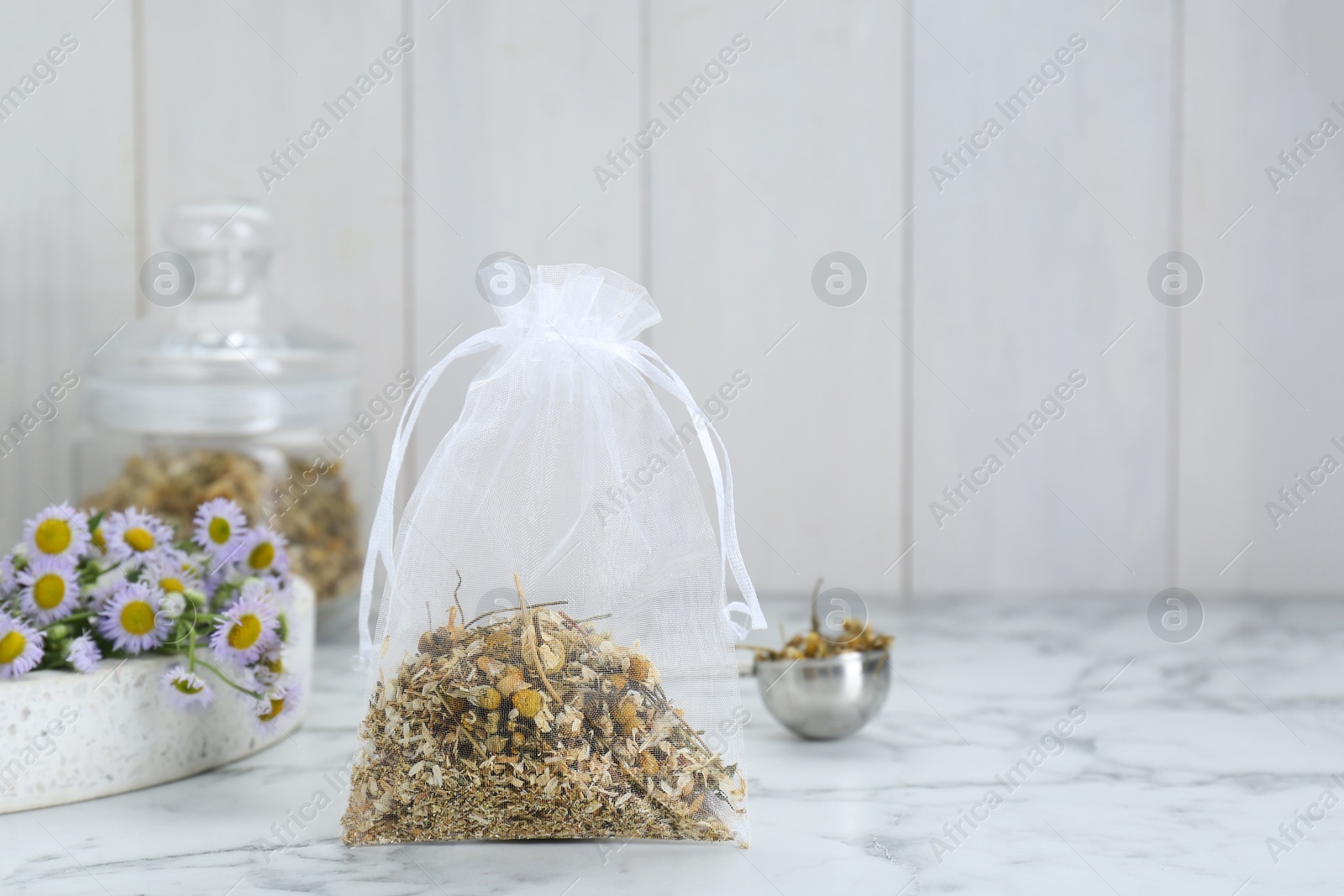 Photo of Scented sachet with dried chamomile flowers on white marble table, space for text