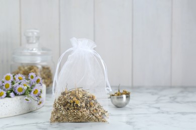 Photo of Scented sachet with dried chamomile flowers on white marble table, space for text