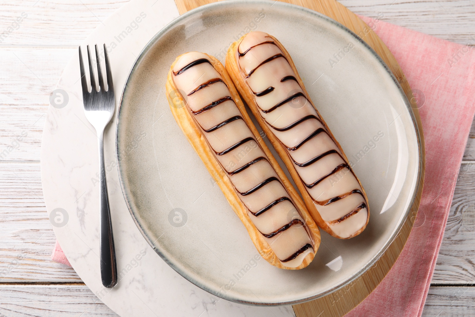 Photo of Tasty glazed eclairs served on wooden rustic table, top view