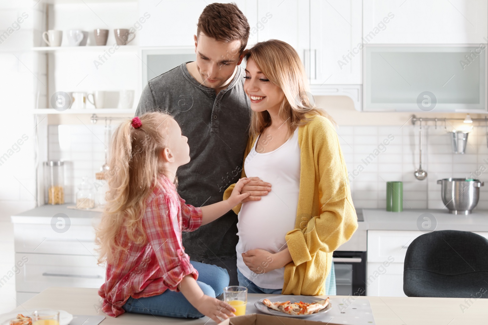 Photo of Pregnant woman and her family eating pizza in kitchen