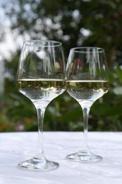 Photo of Glasses of white wine served on marble table outdoors