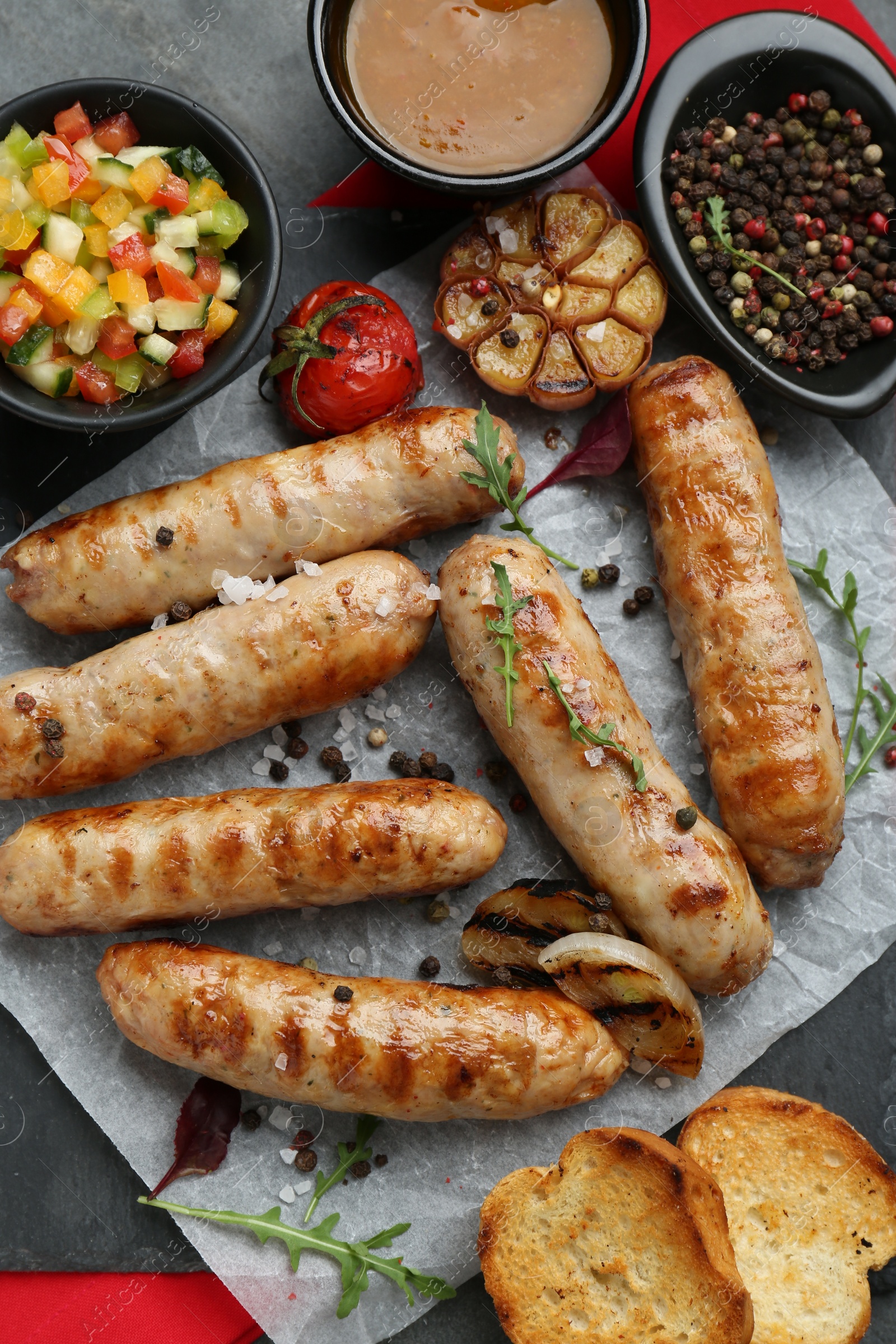 Photo of Tasty fresh grilled sausages with vegetables on grey table, flat lay