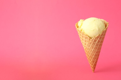 Photo of Delicious yellow ice cream in waffle cone on pink background. Space for text