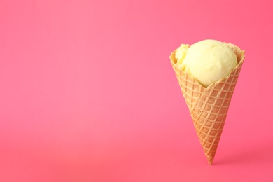 Delicious yellow ice cream in waffle cone on pink background. Space for text