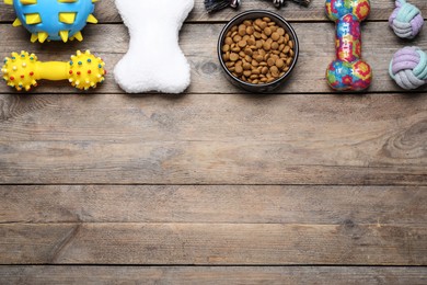 Different pet toys and feeding bowl on wooden background, flat lay. Space for text