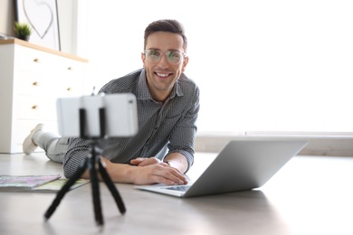 Young blogger with laptop recording video on floor at home