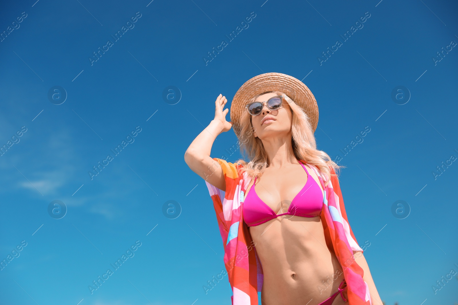 Photo of Sexy young woman in stylish bikini and cover up with accessories against blue sky on sunny day, low angle view. Space for text