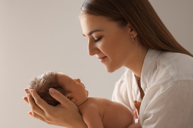 Mother holding her newborn baby on light grey background