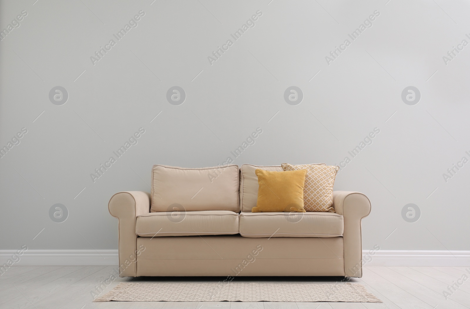 Photo of Comfortable beige sofa near light wall indoors, space for text. Simple interior