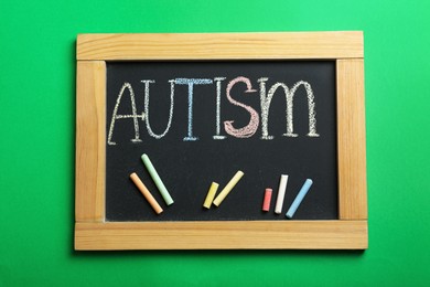 Photo of Blackboard with word Autism and colorful chalks on green background, top view