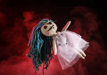 Photo of Female voodoo doll with pins and smoke on red background