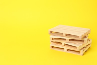 Photo of Stack of wooden pallets on yellow background, space for text